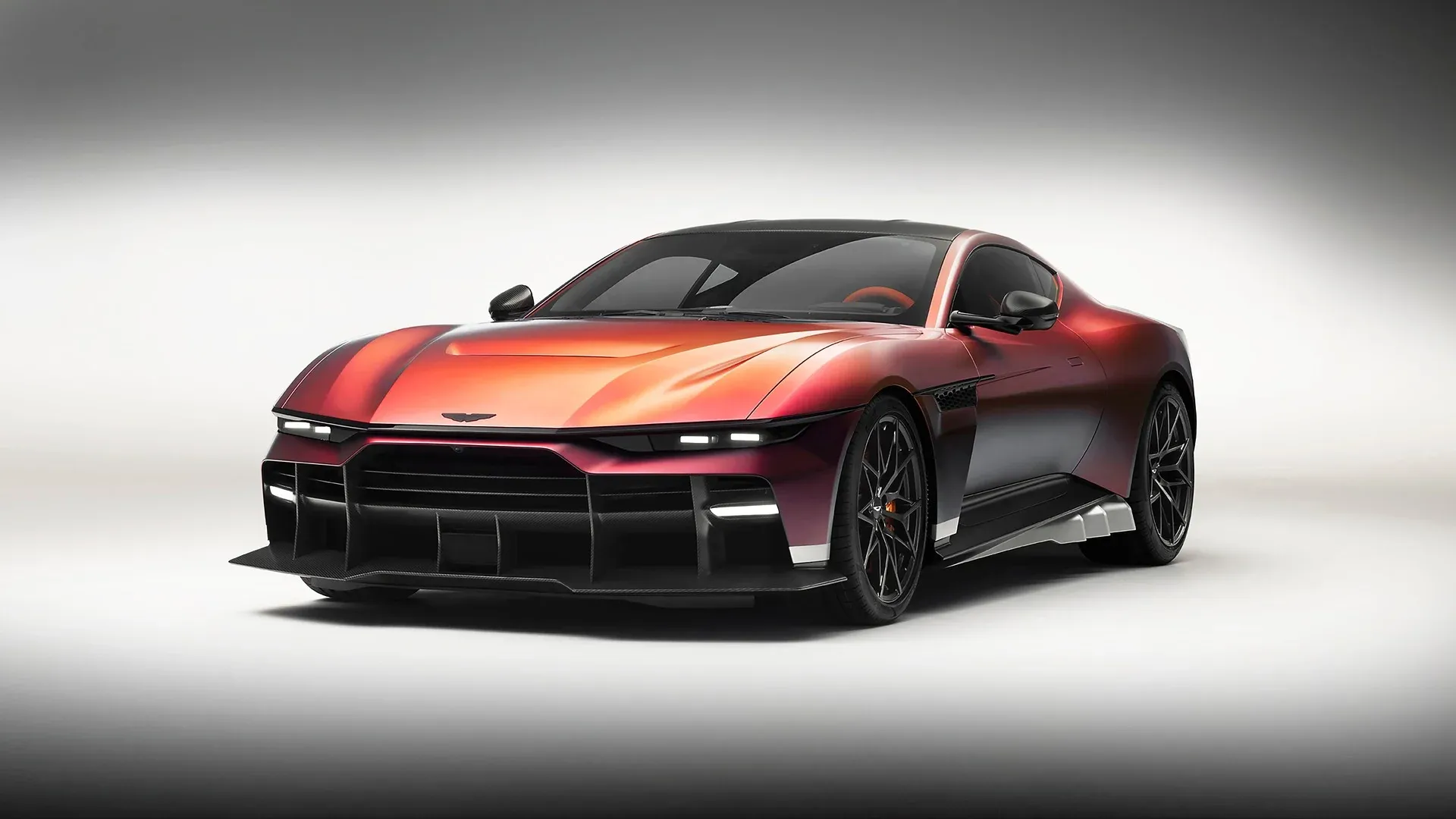 The Aston Martin Valen in a red to purple graduated finish, seen from the front three-quarter in a white studio, its carbon front splitter and black wheels visible