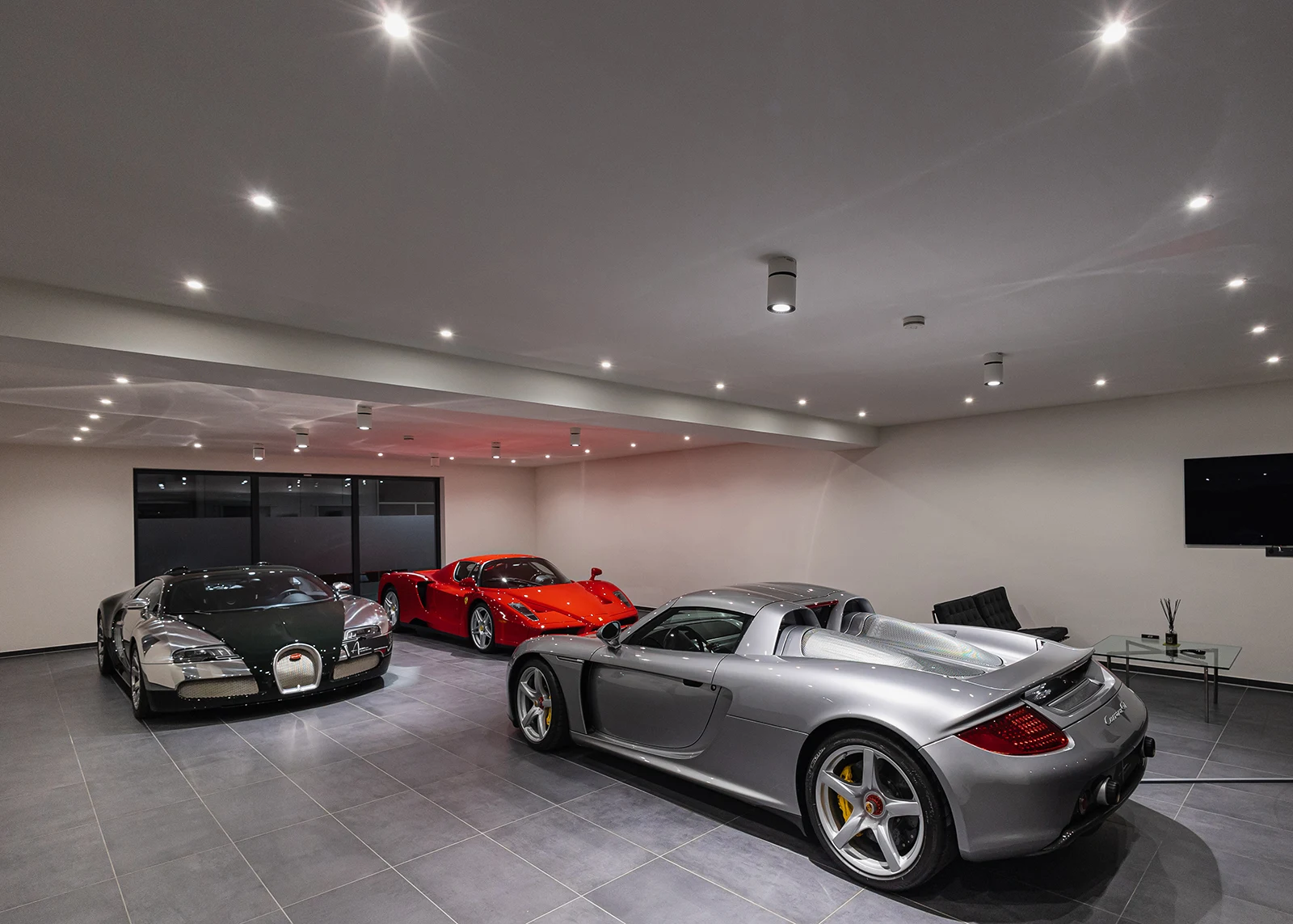 The Amian Collection Cars showroom in Kerpen seen down its length, a Bugatti Veyron, a Ferrari Enzo and a Porsche Carrera GT parked on the grey tiled floor beneath a run of ceiling spotlights
