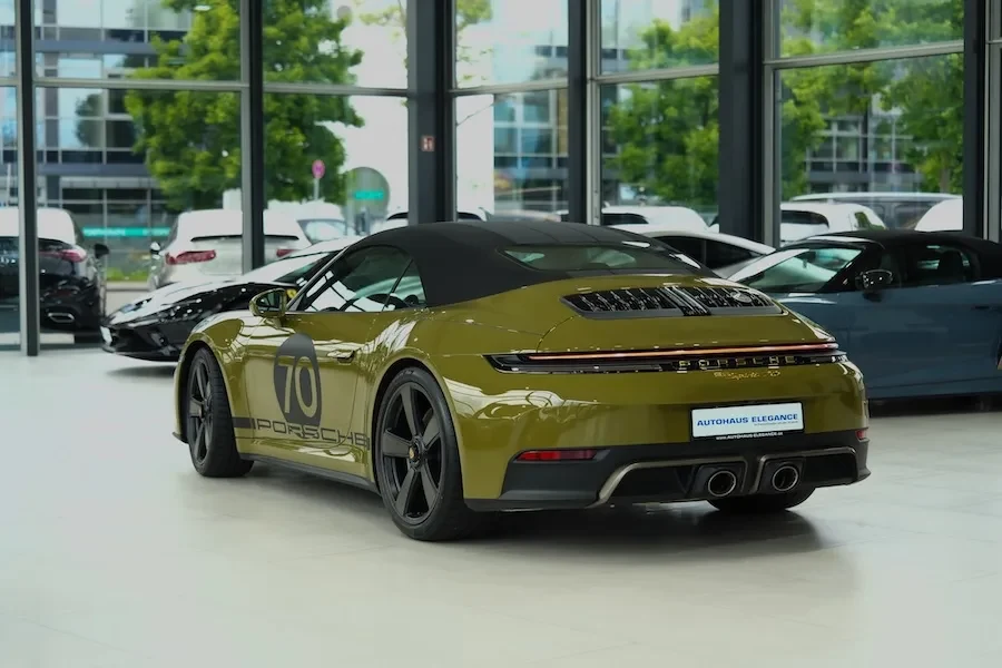 Ein olivgrünes Porsche 911 Cabriolet mit der Nummer 70 auf den Türen, in der Dreiviertelansicht von hinten im Showroom von Autohaus Elegance in Köln, dahinter weitere Fahrzeuge