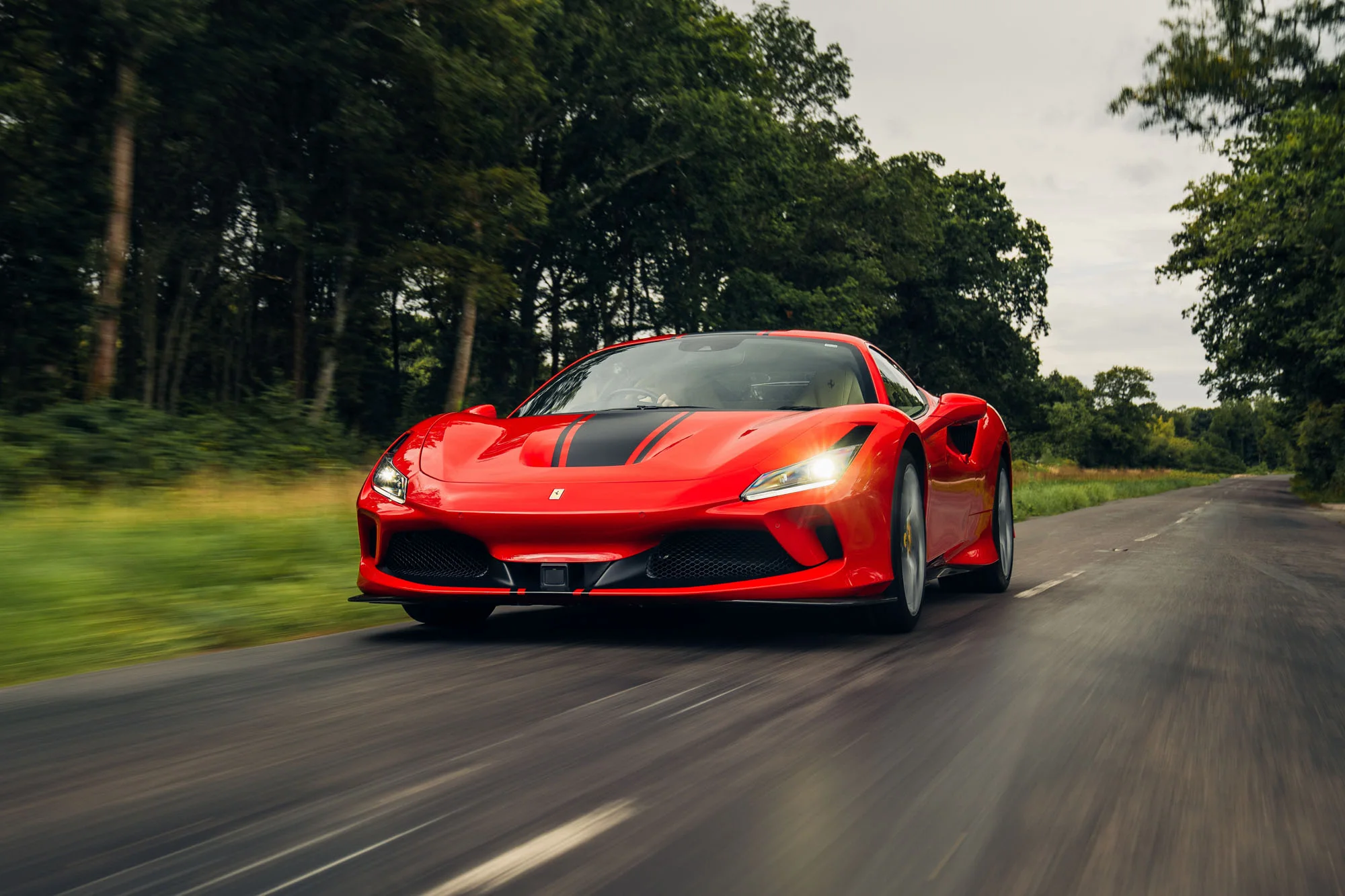 Ein roter Ferrari F8 Tributo in Fahrt auf einer von Bäumen gesäumten Landstraße