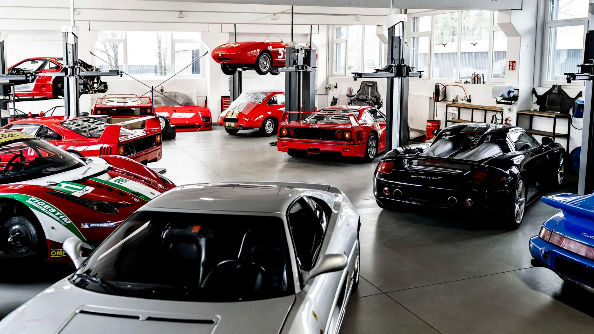 The CarTech Knowledge workshop in Ismaning, with Ferrari and Porsche cars on the lifts and a silver Ferrari in the foreground