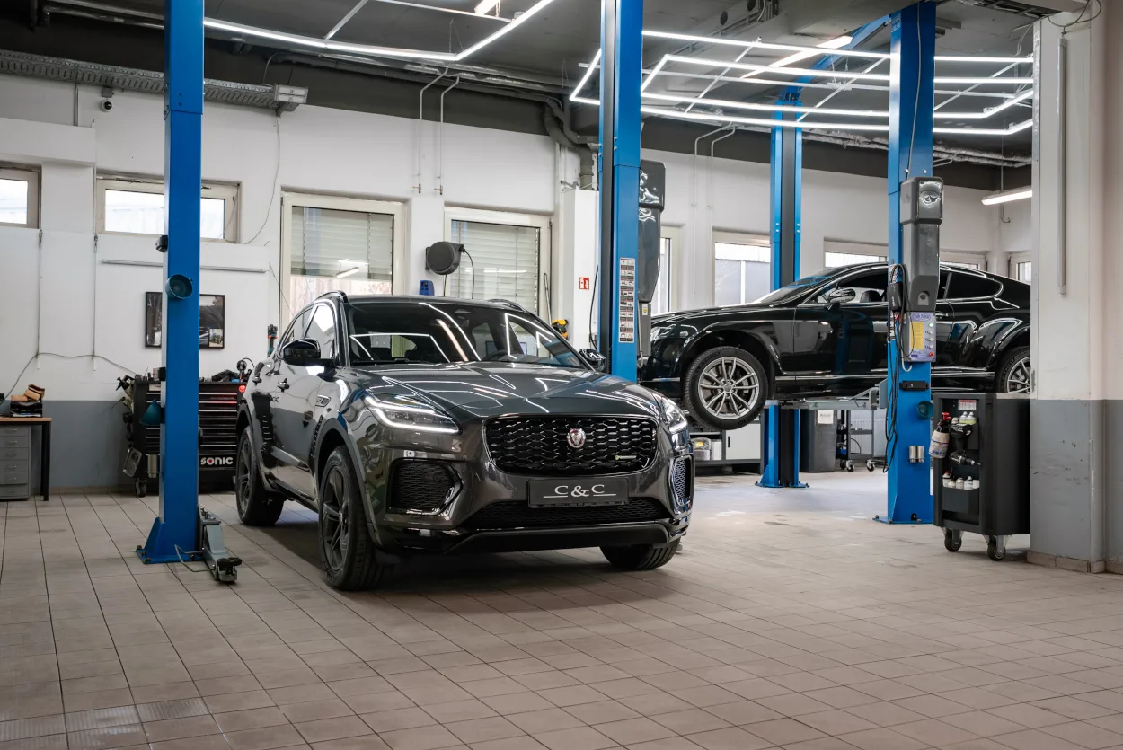 The C&C Premium Cars workshop hall, a dark grey Jaguar SUV standing on the tiled floor between blue two-post lifts while a black saloon is raised on the lift behind it