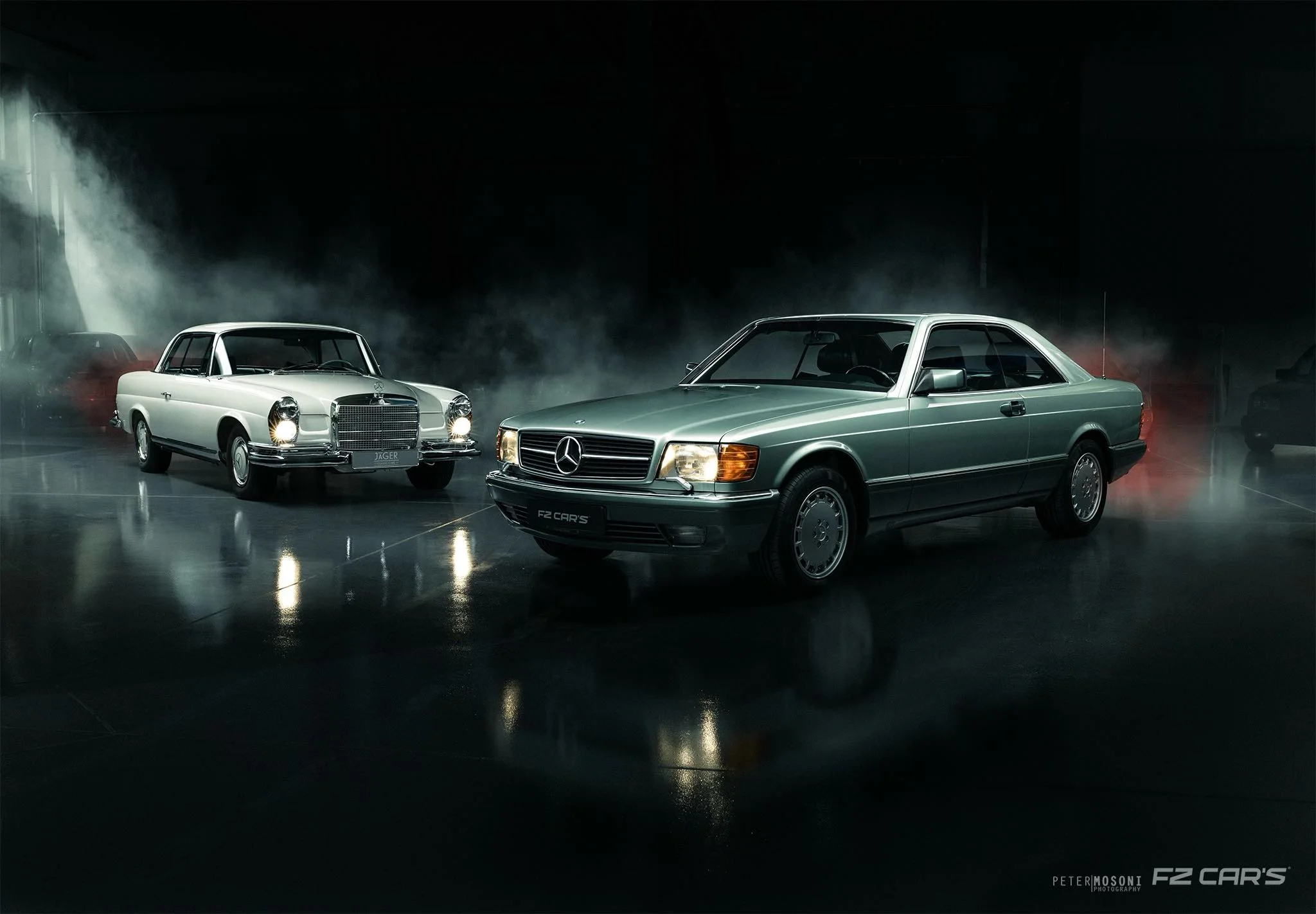 Zwei klassische Mercedes-Benz Coupés, ein weißes W111 und ein silbergrünes 560 SEC, im Studio von FZ Cars in Budapest, gedämpftes Licht und Nebel