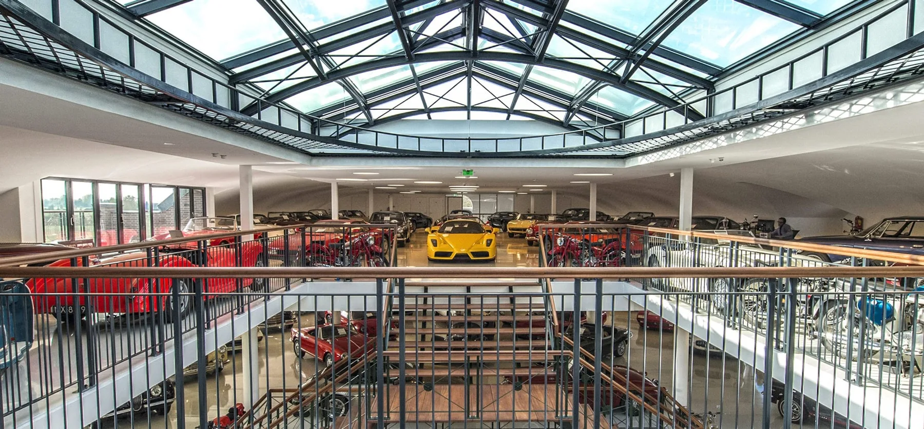 The glass-roofed atrium of the Gallery Aaldering showroom in Brummen, a yellow Ferrari Enzo on the upper floor among classic cars and motorcycles, more classics on the floor below