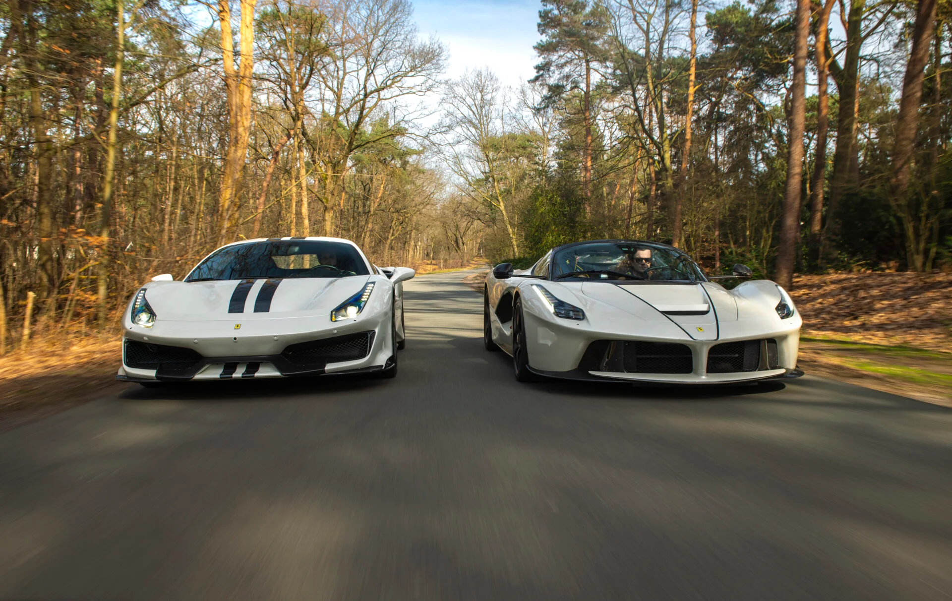 Ein weißer Ferrari 488 Pista und ein weißer LaFerrari fahren auf einer Waldstraße auf die Kamera zu