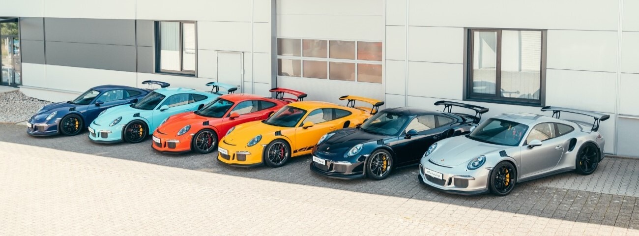 Six Porsche sportives alignées devant le showroom d'un concessionnaire spécialisé