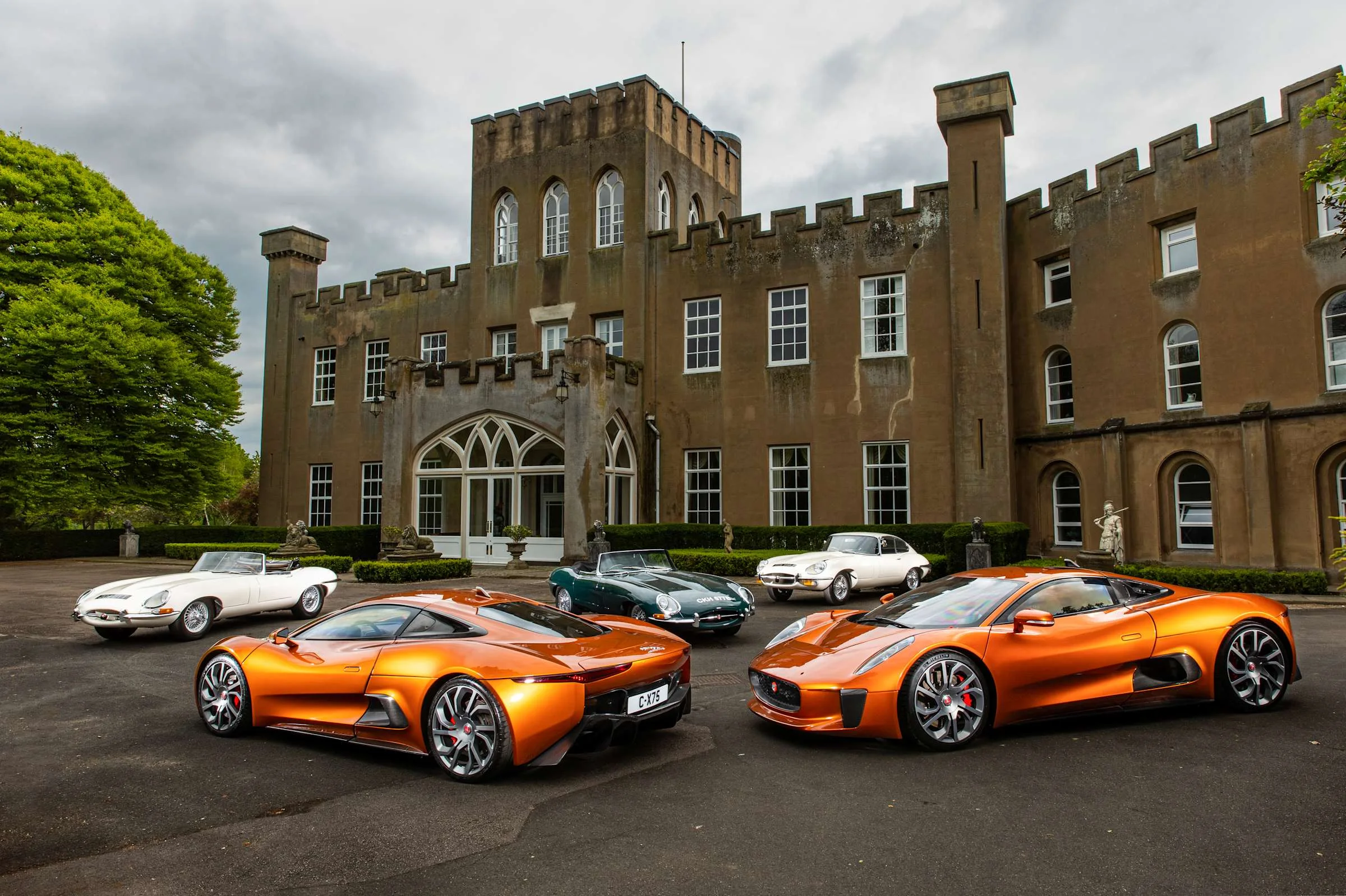 Zwei orangefarbene Jaguar C-X75 und weitere Sportwagen vor der zinnenbewehrten Fassade von Tollerton Hall