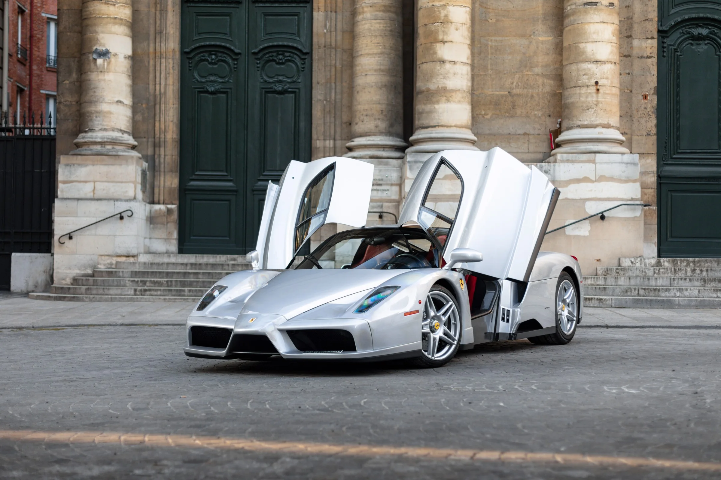 Une Ferrari Enzo argentée, portes ouvertes, devant une façade en pierre à Paris