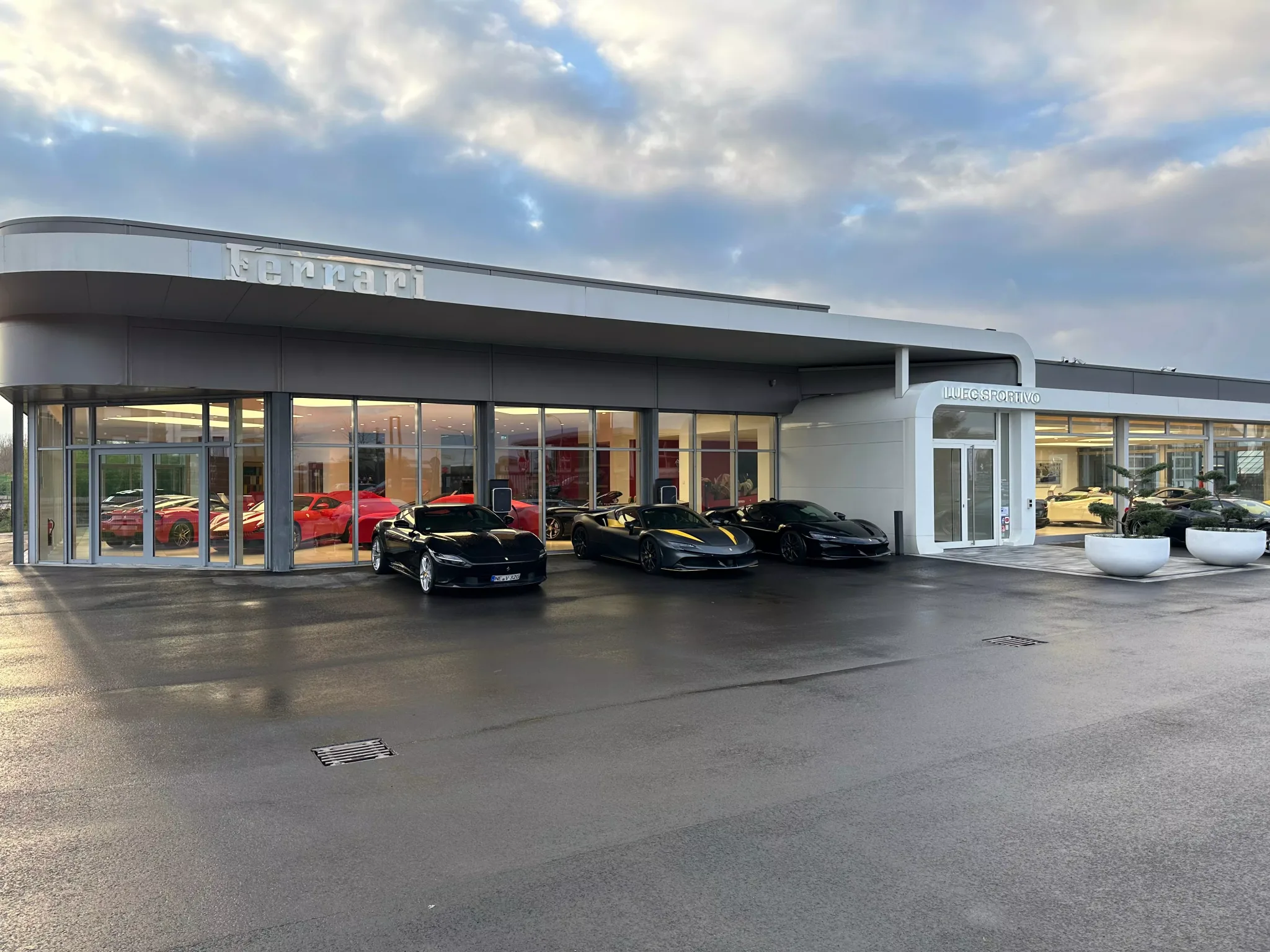 La concession Ferrari LUEG Sportivo à Meerbusch au crépuscule, son showroom vitré éclairé de l'intérieur et trois Ferrari sombres garées sur le parvis