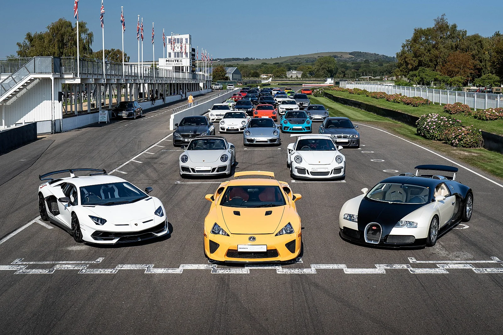 A grid of supercars on the Goodwood circuit, with a Lamborghini Aventador SVJ, a Lexus LFA and a Bugatti Veyron in front