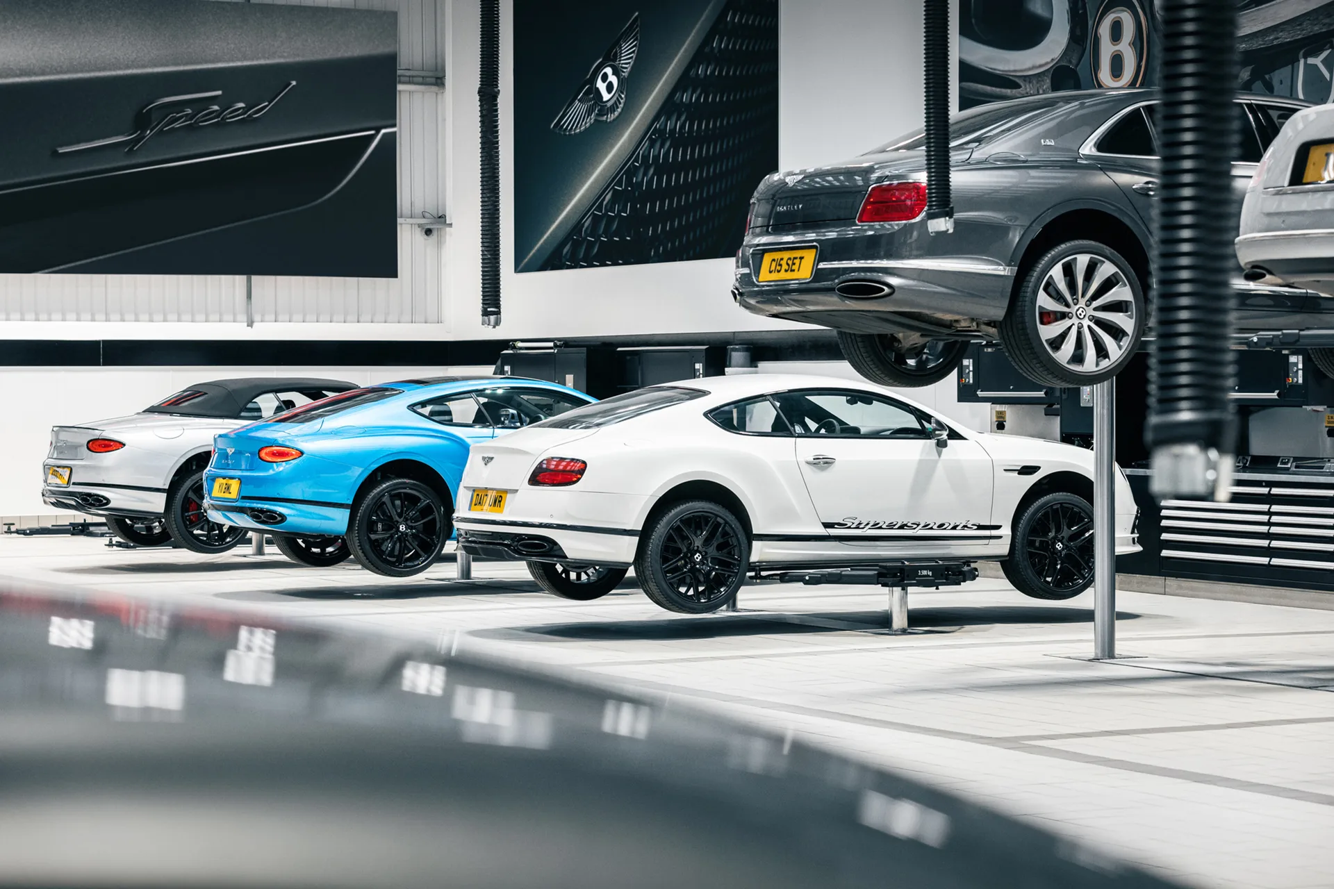 Continental GT auf den Hebebühnen der Bentley-Werkstatt, im Vordergrund ein Supersports in Weiß, darüber ein angehobener Flying Spur