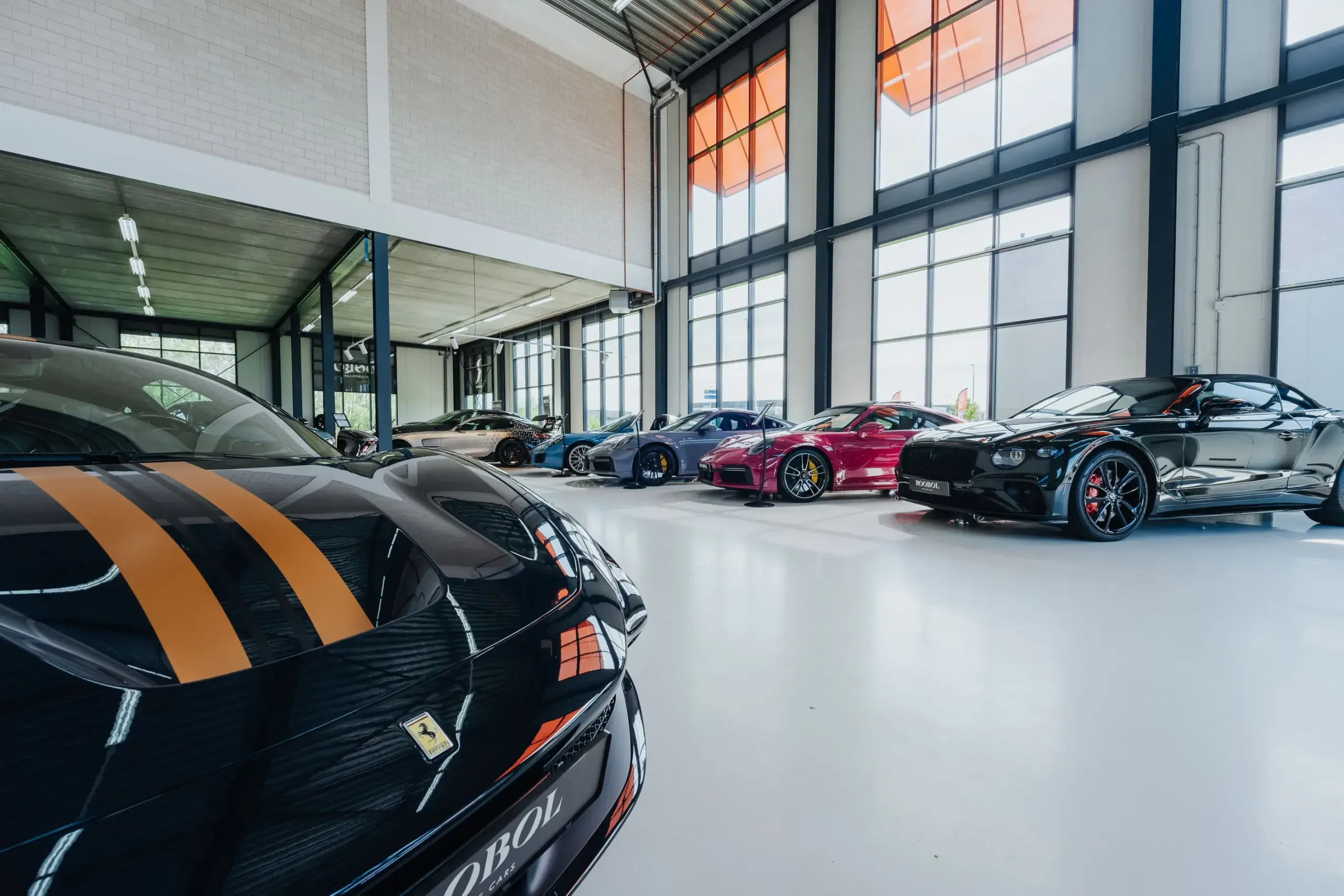 Im Showroom von Roobol Exclusive Cars in Berkel en Rodenrijs, vorn ein schwarzer Ferrari mit orangen Streifen, dahinter eine Reihe Sportwagen an der Glasfront