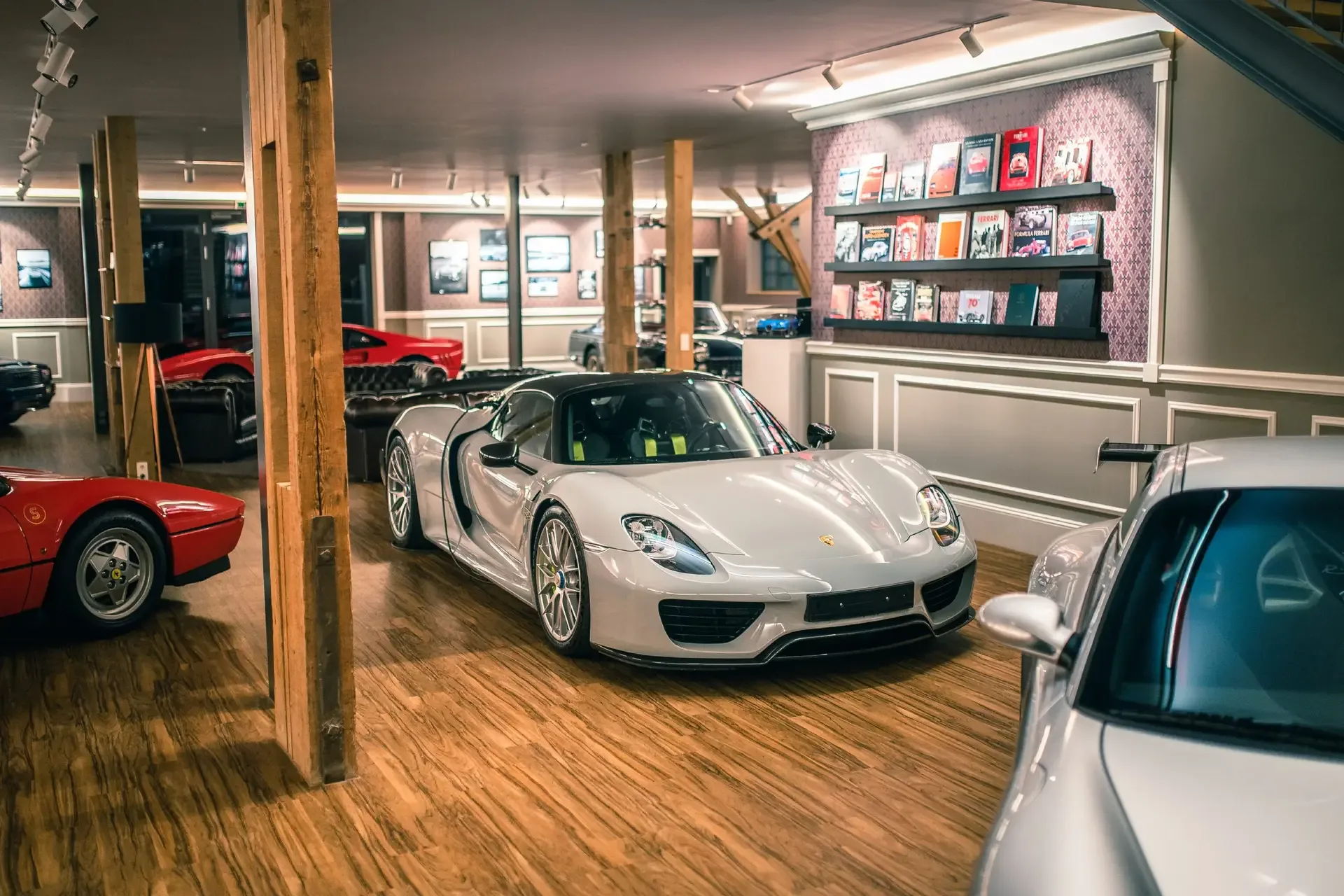 Der Showroom von Schaltkulisse bei München, ein silberner Porsche 918 Spyder auf Holzboden, dahinter ein roter Ferrari und rechts eine Wand mit Automobilbüchern