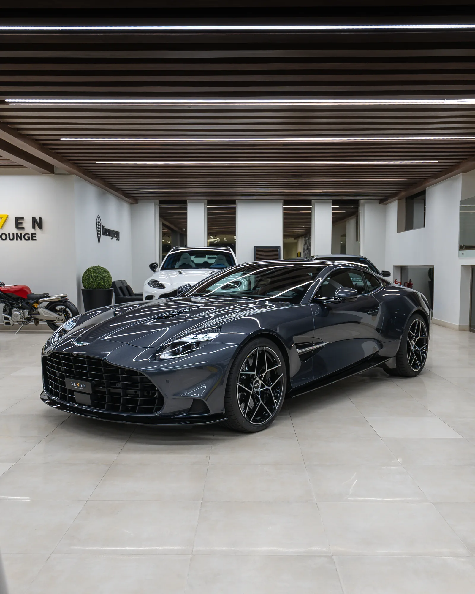 Dunkelgraues Aston Martin Vanquish Coupé, Dreiviertelansicht von vorn im Showroom von SEVEN Car Lounge in Riad
