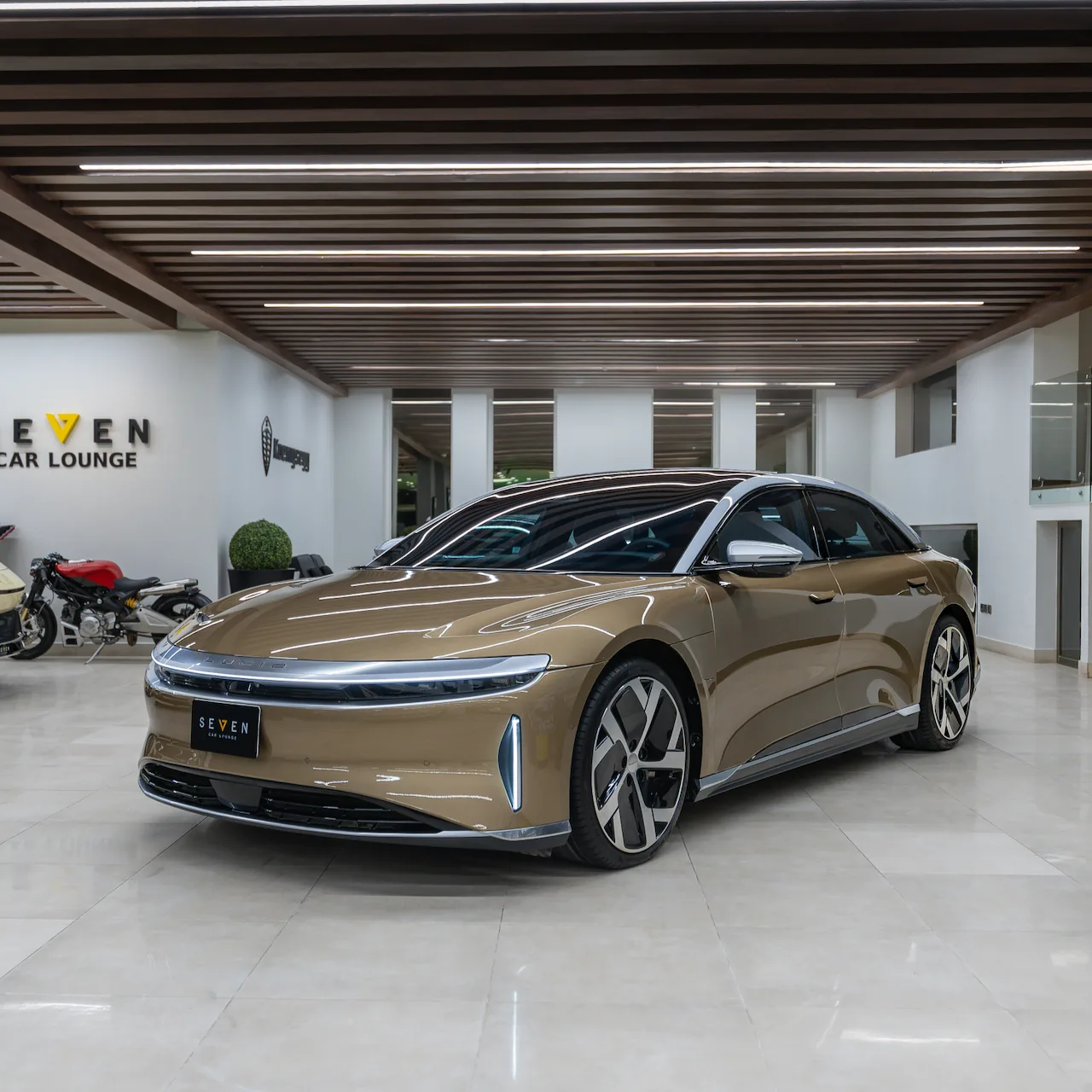 Goldfarbener Lucid Air Dream Edition, Dreiviertelansicht von vorn im Showroom von SEVEN Car Lounge in Riad